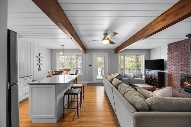 5012 Green Acre Dr, Frederic, MI 49733 - living area with light wood-style flooring, beamed ceiling, a ceiling fan, and wood walls