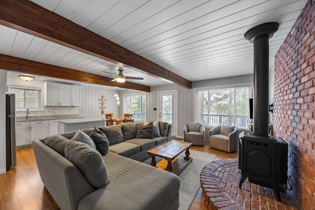 5012 Green Acre Dr, Frederic, MI 49733 - living area with a wood stove, plenty of natural light, light wood finished floors, a ceiling fan, and beamed ceiling