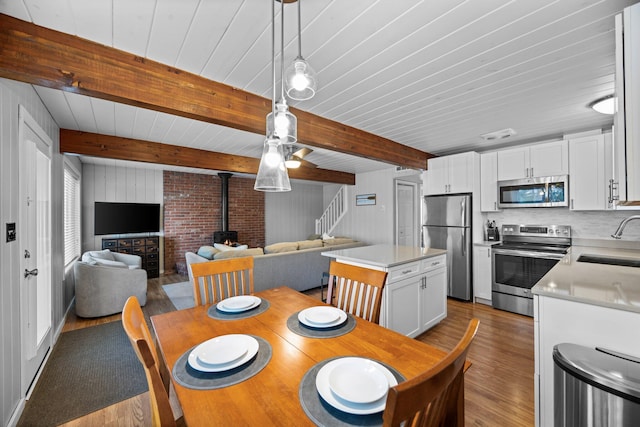 5012 Green Acre Dr, Frederic, MI 49733 - dining area featuring a wood stove, wood finished floors, stairs, beam ceiling, and wood walls