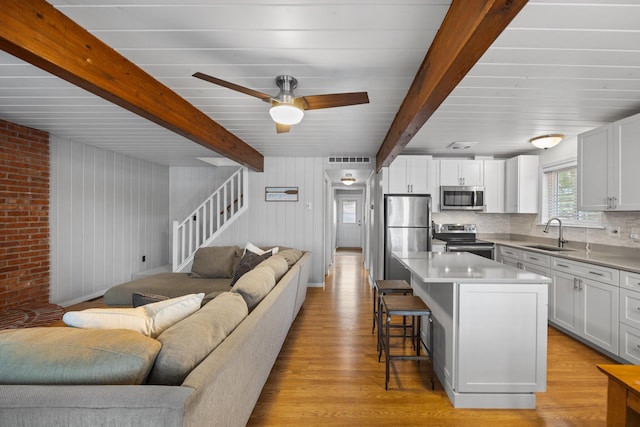 5012 Green Acre Dr, Frederic, MI 49733 - living room with light wood-type flooring, beam ceiling, ceiling fan, and stairway