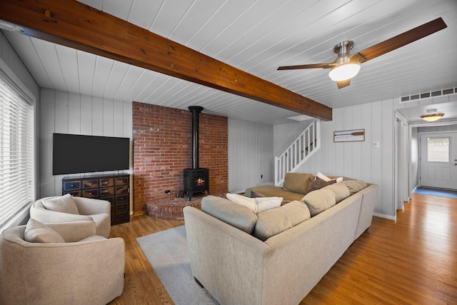 5012 Green Acre Dr, Frederic, MI 49733 - living room with wood finished floors, a wood stove, stairs, beam ceiling, and ceiling fan