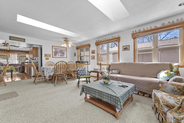 living area with a ceiling fan, carpet flooring, and a skylight