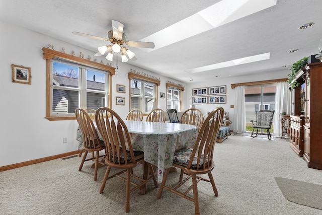 dining room featuring visible vents, baseboards, light colored carpet, a textured ceiling, and a skylight