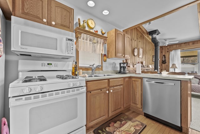 kitchen featuring a peninsula, white appliances, light wood-type flooring, light countertops, and a sink