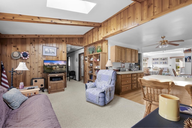 living room featuring wooden walls, a ceiling fan, a skylight, and beam ceiling
