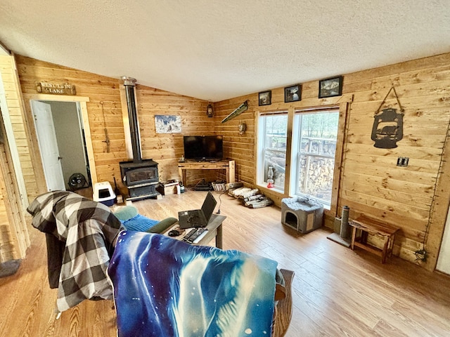 3313 Pleasant View Dr, Lewiston, MI 49756 - living area with lofted ceiling, hardwood / wood-style floors, wood walls, a wood stove, and a textured ceiling