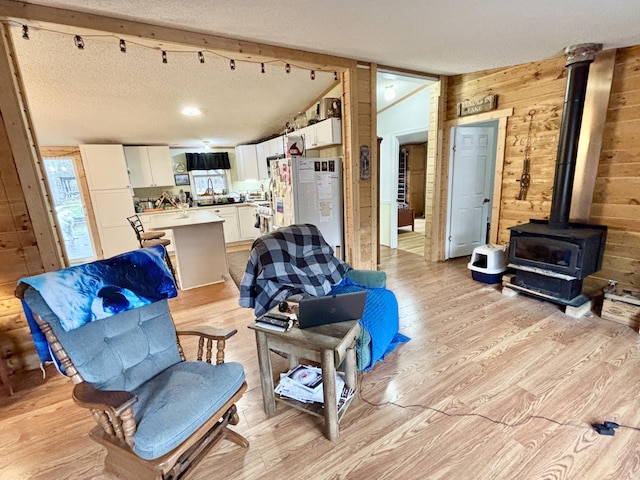 3313 Pleasant View Dr, Lewiston, MI 49756 - living room with wooden walls, a wood stove, light wood-style floors, a textured ceiling, and lofted ceiling