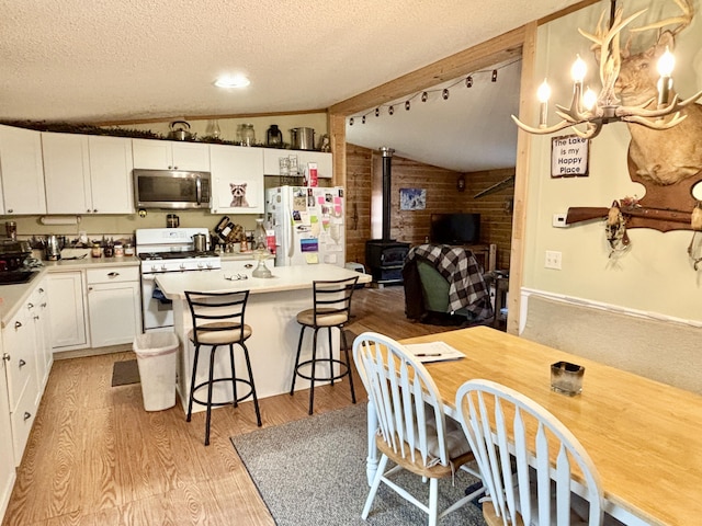 3313 Pleasant View Dr, Lewiston, MI 49756 - kitchen featuring white appliances, vaulted ceiling, a wood stove, light wood-style floors, and a textured ceiling