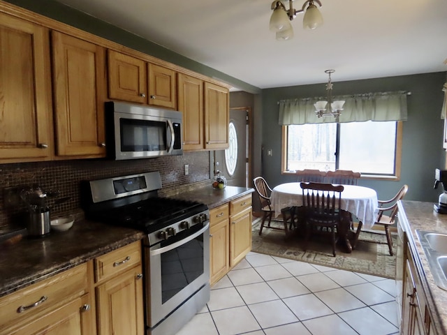 kitchen with appliances with stainless steel finishes, backsplash, a notable chandelier, and dark countertops