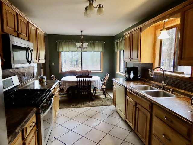 kitchen featuring appliances with stainless steel finishes, dark countertops, a sink, a notable chandelier, and light tile patterned flooring