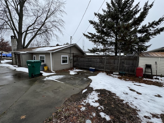 view of snow covered exterior with a garage, fence, an outbuilding, and a chimney