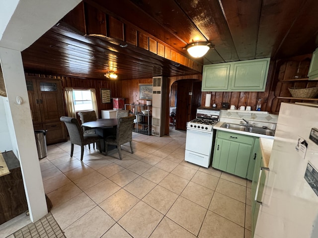 kitchen featuring wooden walls, light tile patterned flooring, green cabinetry, white appliances, and arched walkways
