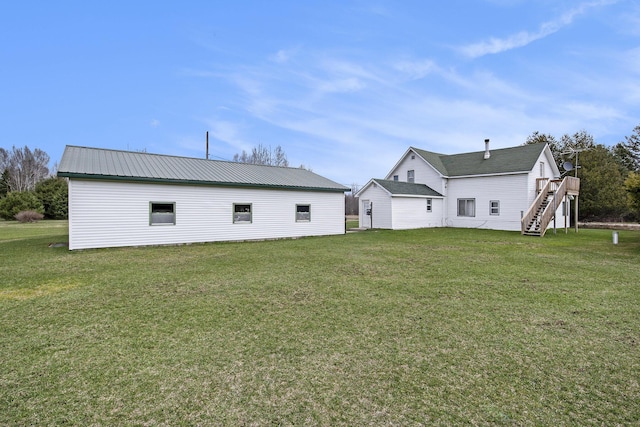 back of house featuring a lawn, metal roof, and stairway
