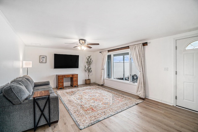 living area featuring light wood-style floors, a ceiling fan, and baseboards