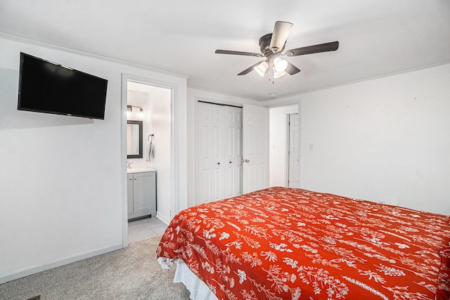 bedroom featuring a closet, baseboards, ensuite bathroom, ceiling fan, and light colored carpet