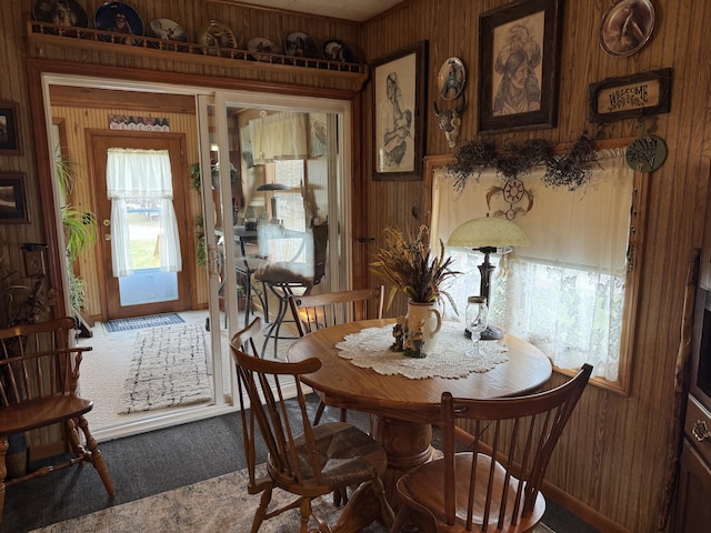 dining area featuring plenty of natural light, carpet, and wood walls