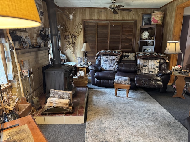 living area with a wood stove, carpet, a ceiling fan, and wood walls