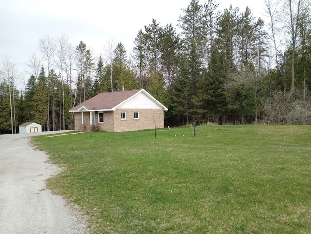 view of side of home featuring driveway, a storage shed, an outbuilding, a wooded view, and a yard