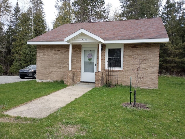 view of front of home with brick siding, roof with shingles, and a front yard