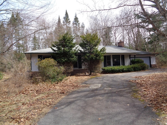 ranch-style home featuring brick siding, a chimney, a garage, and aphalt driveway