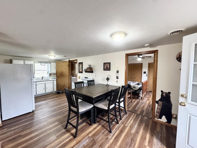 dining area featuring ceiling fan, a textured ceiling, visible vents, and dark wood finished floors