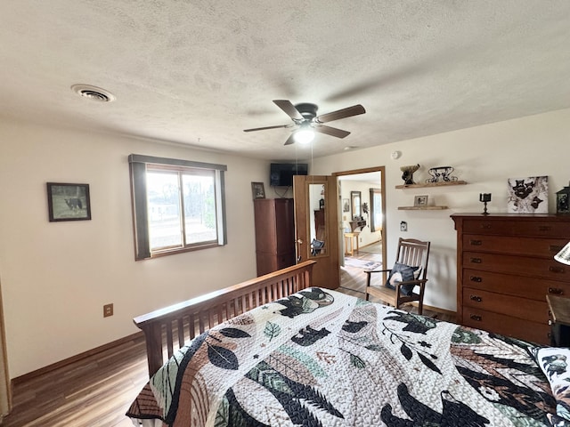 bedroom with baseboards, visible vents, a textured ceiling, and wood finished floors