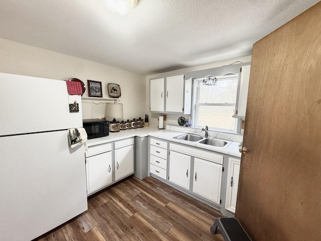kitchen featuring freestanding refrigerator, a sink, black microwave, light countertops, and white cabinets