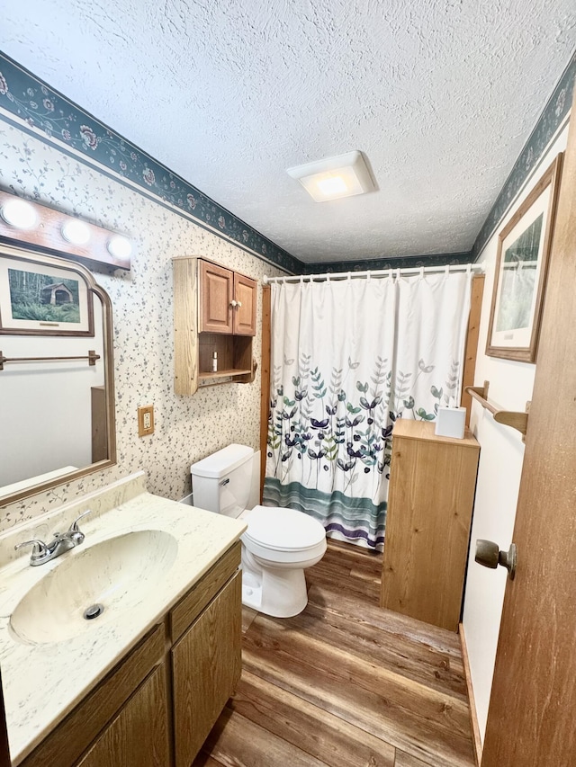 bathroom featuring toilet, wallpapered walls, a textured ceiling, and wood finished floors