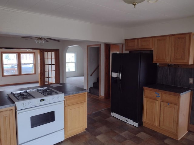 kitchen with dark floors, white gas range, black fridge, arched walkways, and dark countertops