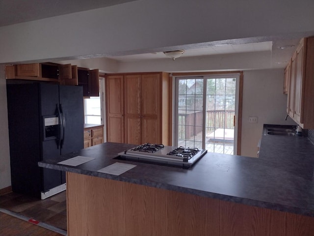 kitchen with a sink, brown cabinets, white gas cooktop, black refrigerator with ice dispenser, and dark countertops