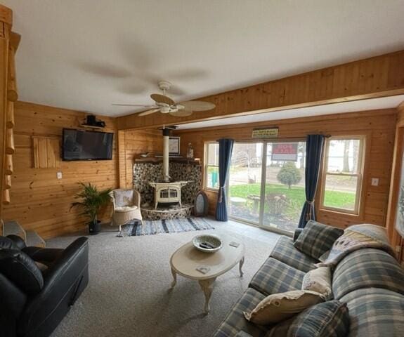 carpeted living area with a wood stove, wooden walls, and a healthy amount of sunlight