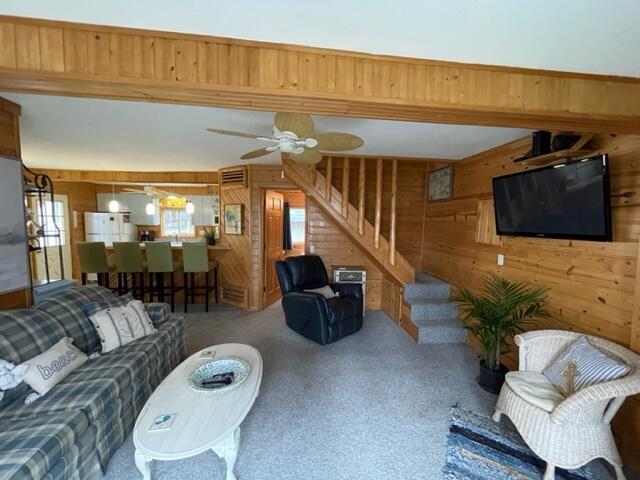 carpeted living area with a wealth of natural light, wood walls, a ceiling fan, and stairway