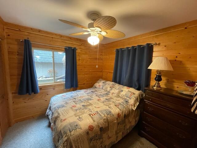 carpeted bedroom featuring wood walls and ceiling fan
