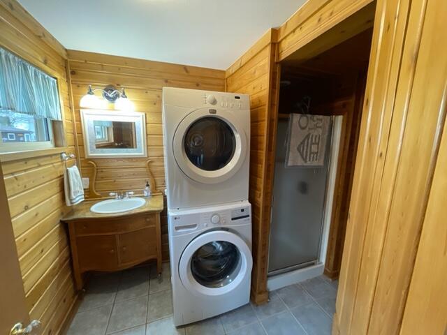 laundry area featuring stacked washer / dryer, wooden walls, a sink, and light tile patterned floors