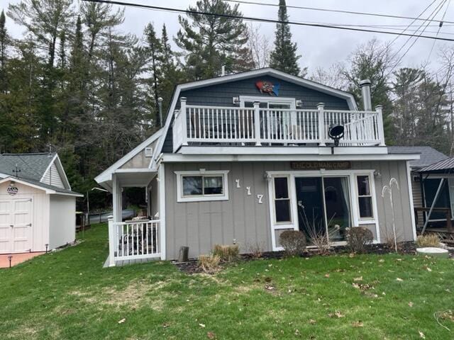back of property featuring a storage shed, a yard, board and batten siding, a balcony, and an outbuilding