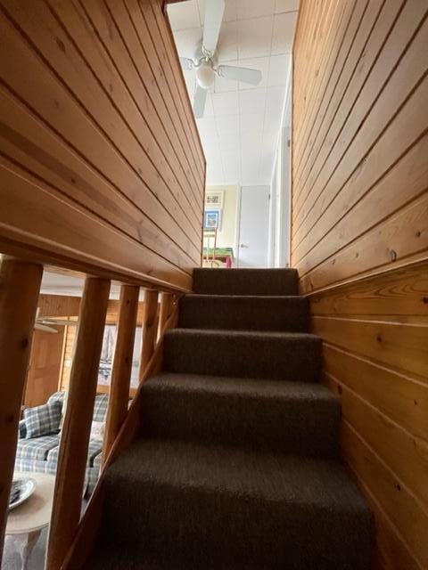 stairway with wooden walls and a ceiling fan