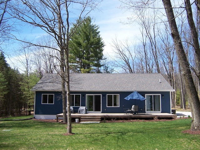 rear view of property featuring a shingled roof, a yard, and a wooden deck