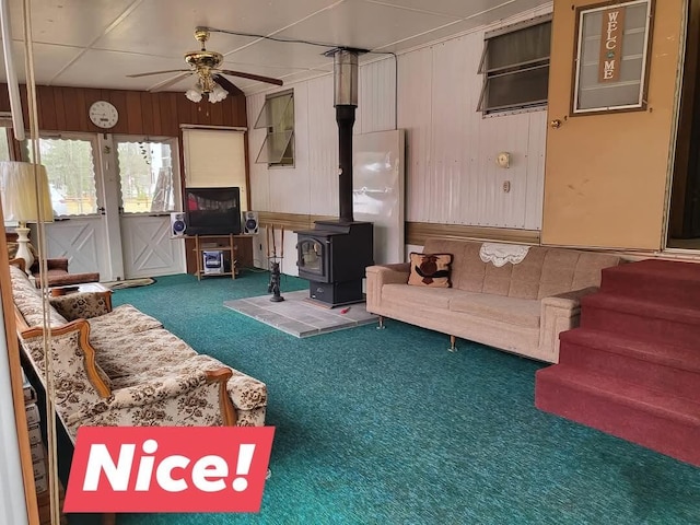 10675 N Shady Ln, Irons, MI 49644 - living area featuring a ceiling fan, a wood stove, wood walls, and carpet