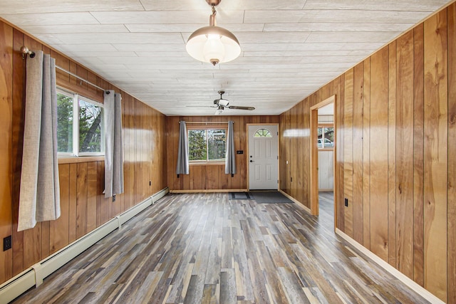 interior space with wood finished floors, a ceiling fan, baseboards, wooden walls, and a baseboard radiator