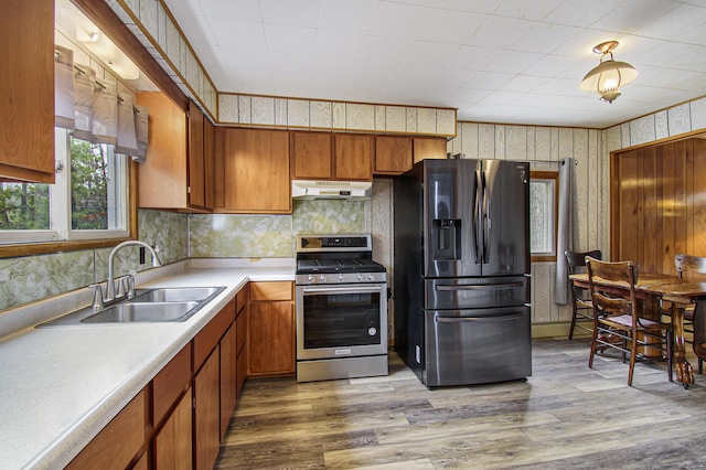 kitchen with stainless steel gas range oven, under cabinet range hood, refrigerator with ice dispenser, a sink, and wood finished floors