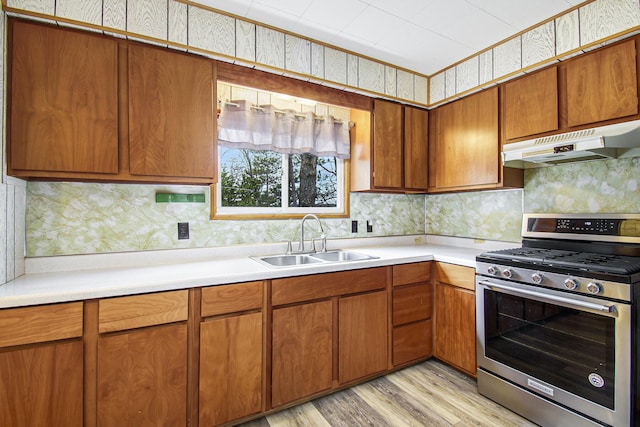 kitchen featuring light wood-style flooring, a sink, stainless steel range with gas cooktop, under cabinet range hood, and light countertops