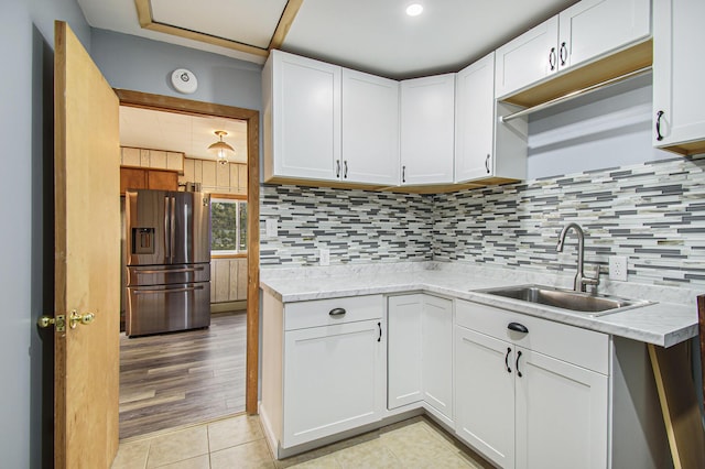 kitchen featuring a sink, tasteful backsplash, stainless steel refrigerator with ice dispenser, and white cabinets