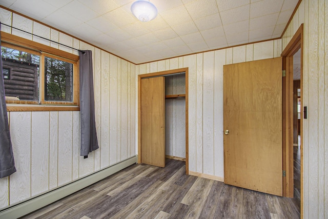 unfurnished bedroom with wood finished floors, a closet, crown molding, wood walls, and a baseboard radiator