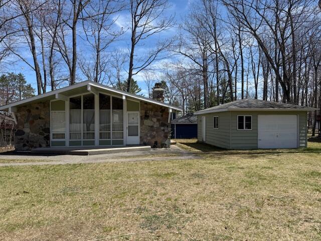 rear view of property featuring a chimney, an outbuilding, a lawn, stone siding, and a garage