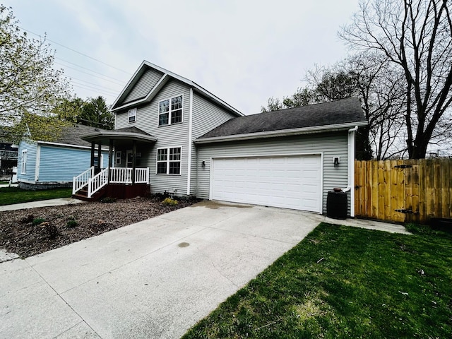 traditional home featuring a porch, fence, an attached garage, driveway, and a front lawn