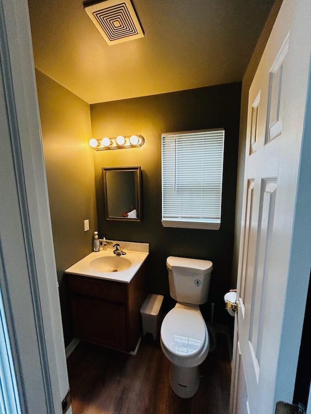 half bathroom featuring toilet, wood finished floors, vanity, visible vents, and baseboards