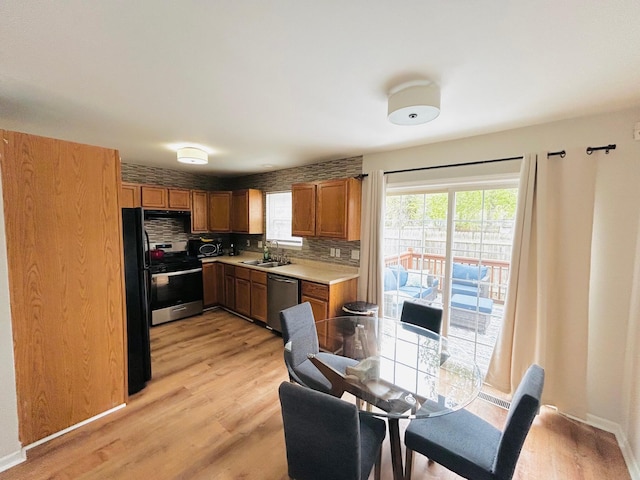 kitchen featuring light wood-style flooring, a sink, stainless steel appliances, backsplash, and light countertops