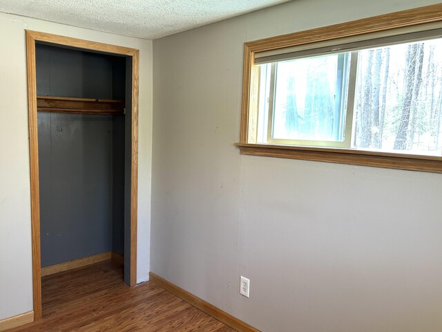 unfurnished bedroom with baseboards, a closet, a textured ceiling, and wood finished floors