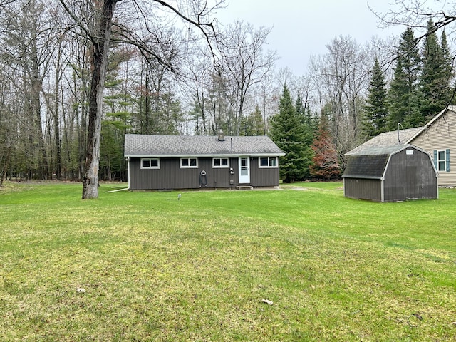 rear view of property with a shingled roof, a yard, an outbuilding, and a storage unit