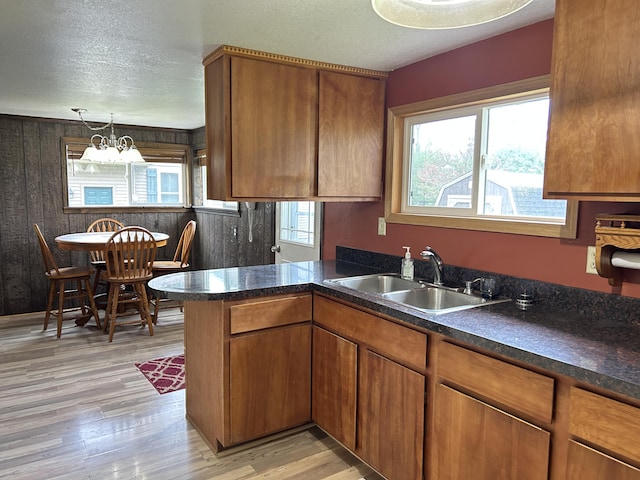 kitchen featuring a sink, brown cabinetry, light wood finished floors, an inviting chandelier, and dark countertops